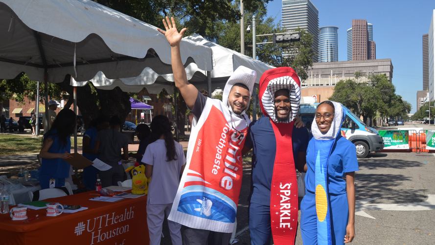 Three dental students stand outdoors in Houston wearing dental-themed costumes.