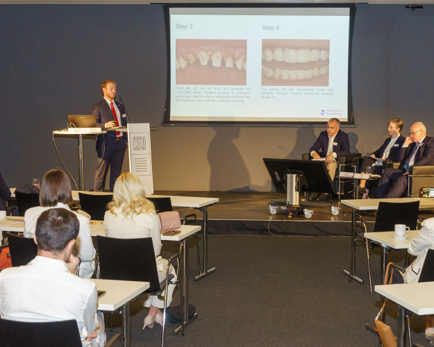 A man is giving a presentation to a panel of judges with in front of an audience.