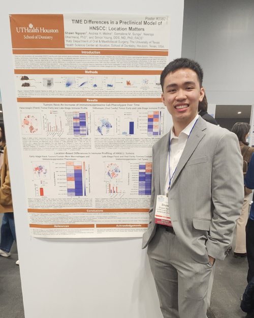Man dressed in business casual attire stands next to displayed poster.
