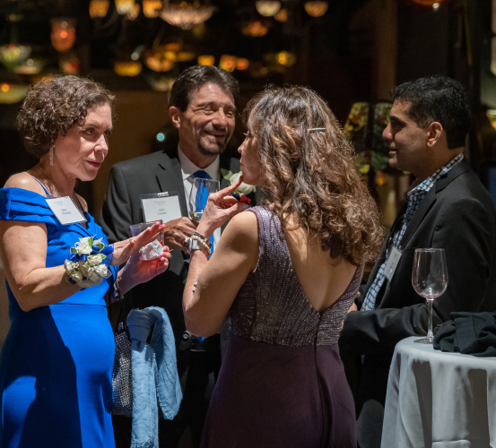 Four people conversing at a formal indoor event with tables and decorative lights.