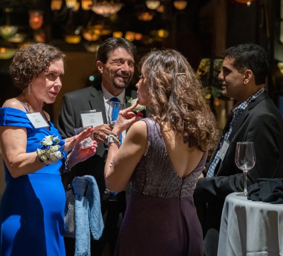 Four people conversing at a formal indoor event with tables and decorative lights.