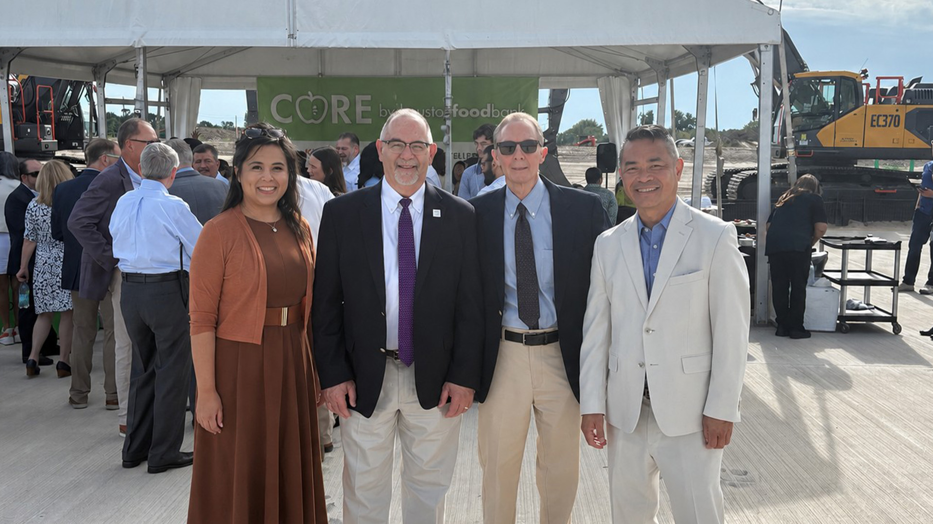 Four event attendees stand together near a tented gathering area during an outdoor event.
