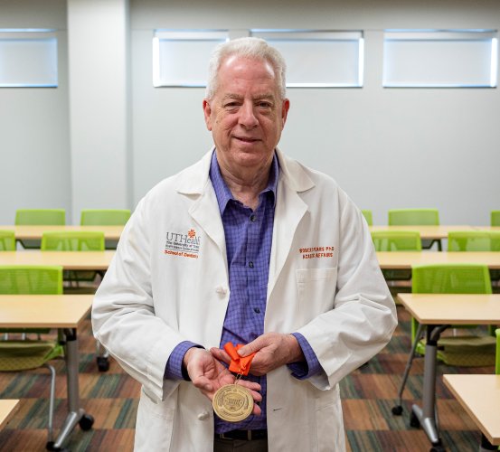 Man in a lab coat poses with a commemorative medal.