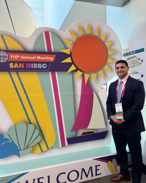 Man in a suit stands in front of an event sign.