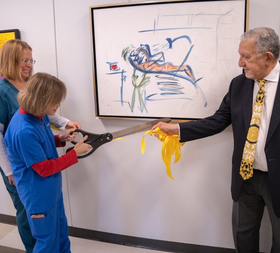 Three individuals cut a ribbon with large scissors.