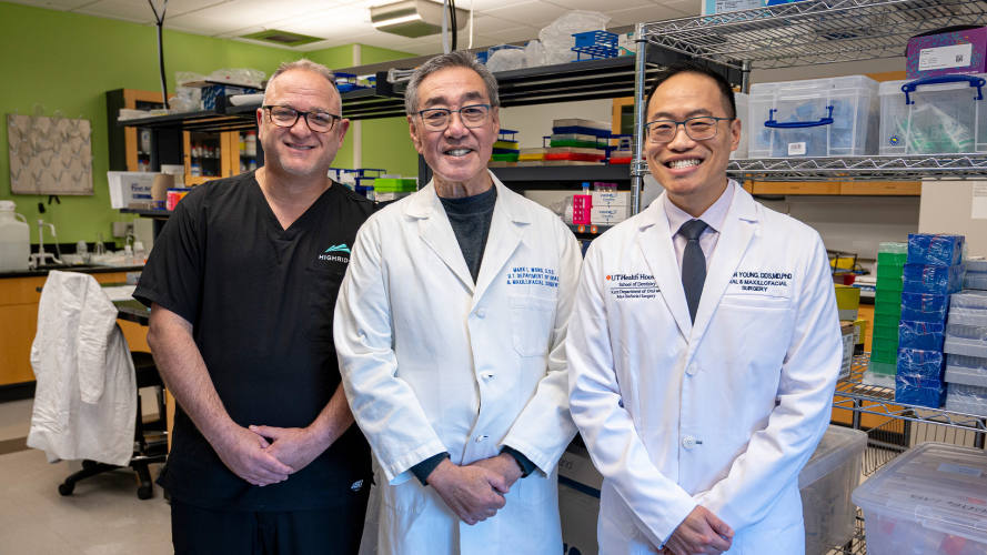 Three researchers in lab coats and scrubs stand in a research lab at UTHealth Houston School of Dentistry.