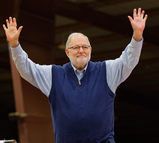 Man stands with arms raised, gesturing to crowd.