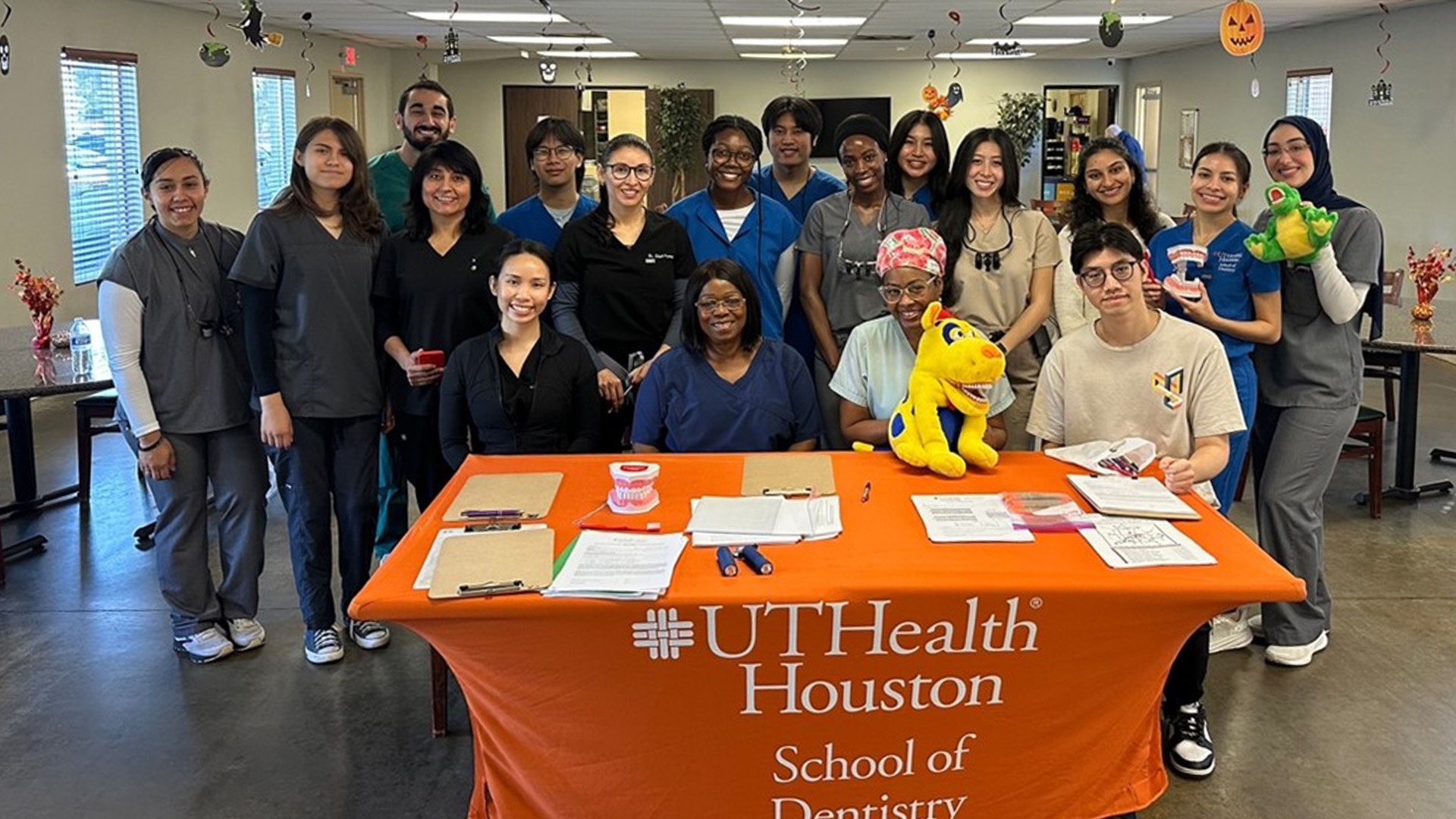 Dental care providers wearing scrubs pose for a group photo around an event table.