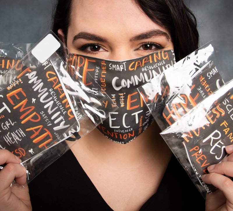 Dr. Ana Ibarra-Noriega wears and holds up several masks made with her design.