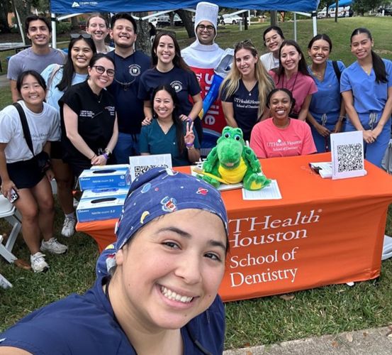 Selfie in front of a group of people standing being a table at an outdoor event.
