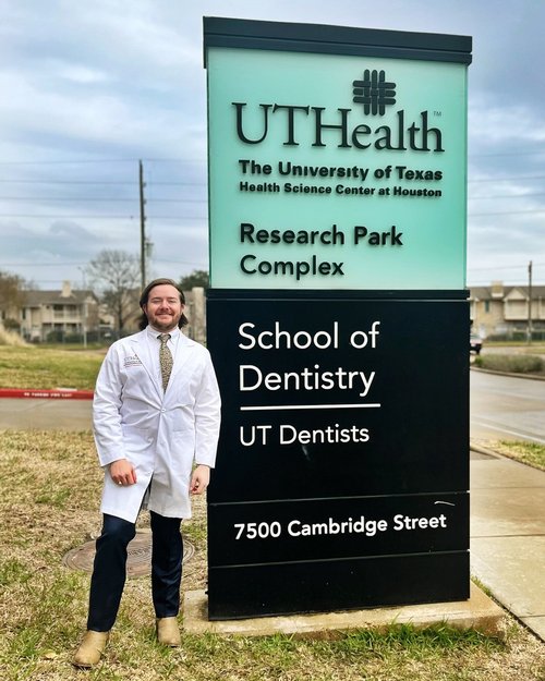 Cooper Mohrmann stands next to the UTHealth Houston School of Dentistry sign following the Dental Class of 2025 White Coat Ceremony.