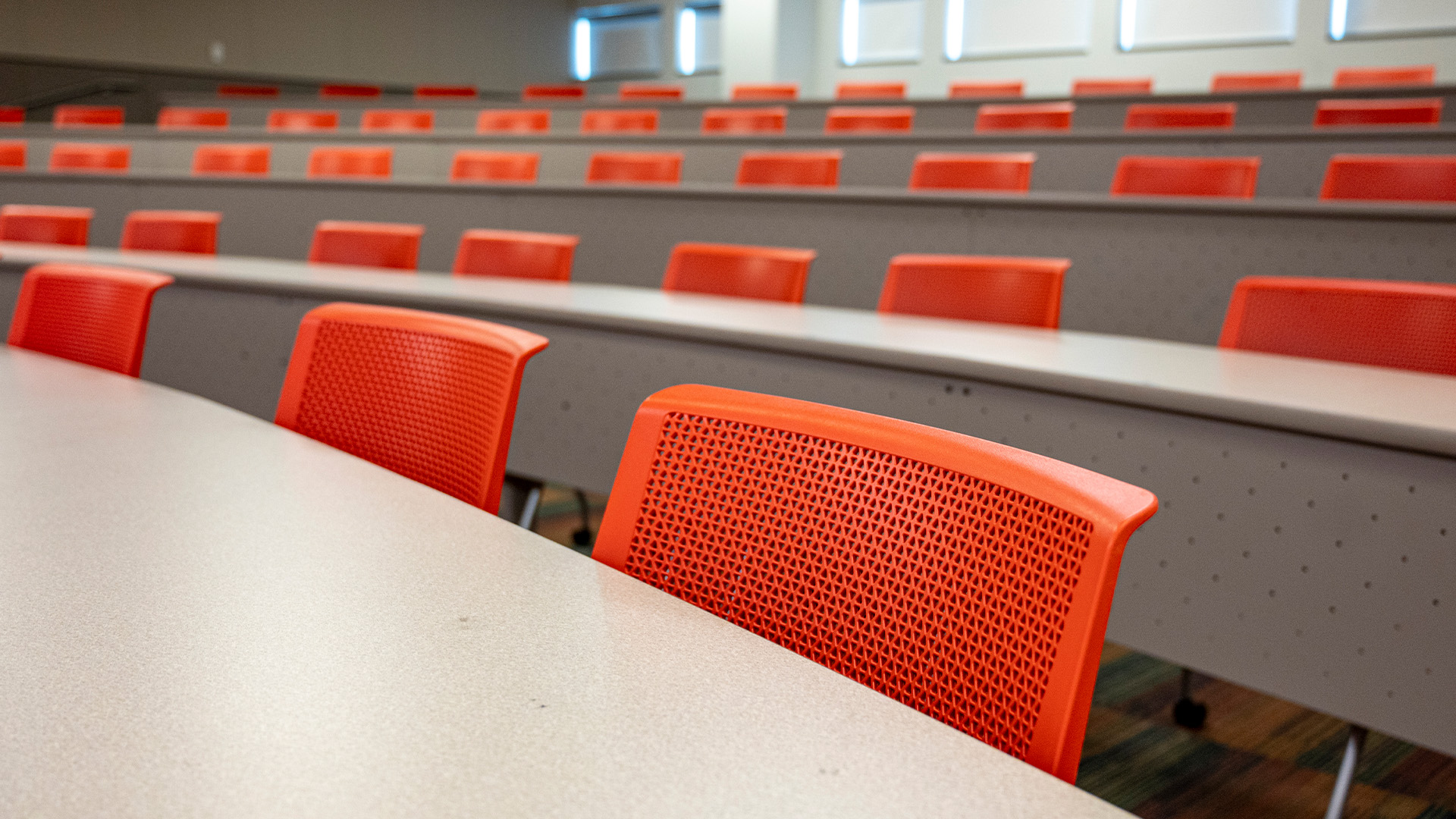 Empty classroom with rows of desks and bright orange chairs.