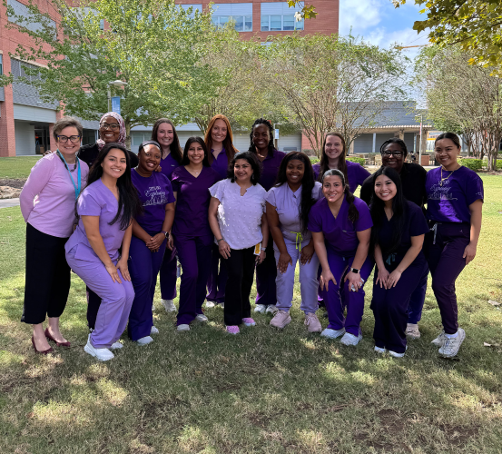 Dental hygiene students and faculty stand for a group photo in a courtyard all wearing purple.