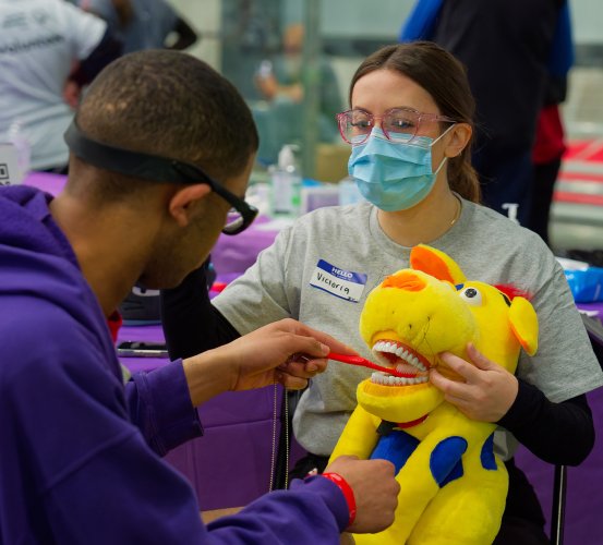 Student volunteer demonstrates oral hygiene practices with a patient using a stuffed animal.