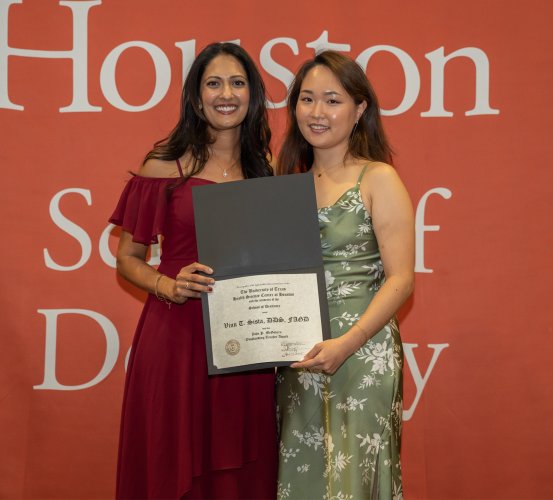 Two people pose with a certificate in front of an orange backdrop.