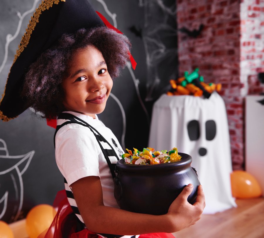 A little girl dressed in a pirate costume holds a bucket of candy.