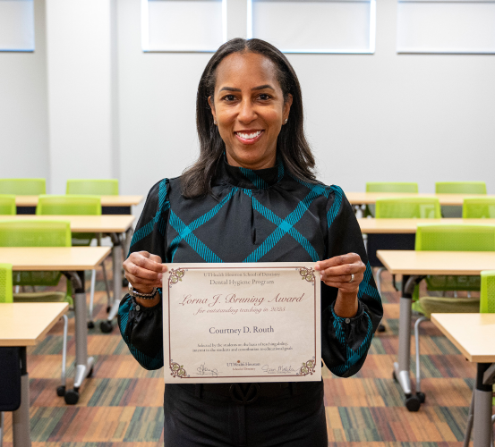 Person holding an award in an empty lecture hall with green seats.