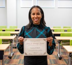 Two people pose with a certificate in front of an orange backdrop.