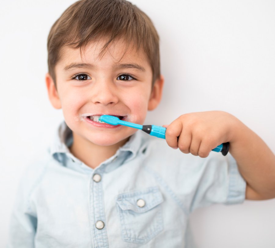 Child brushes his teeth with a bright blue toothbrush, in observance of National Children's Dental Health Month.