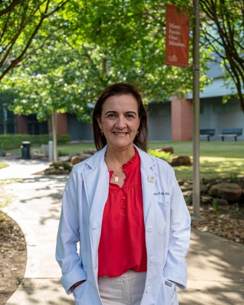 Dentists stands with hands in white coat pockets under a tree-covered walkway.