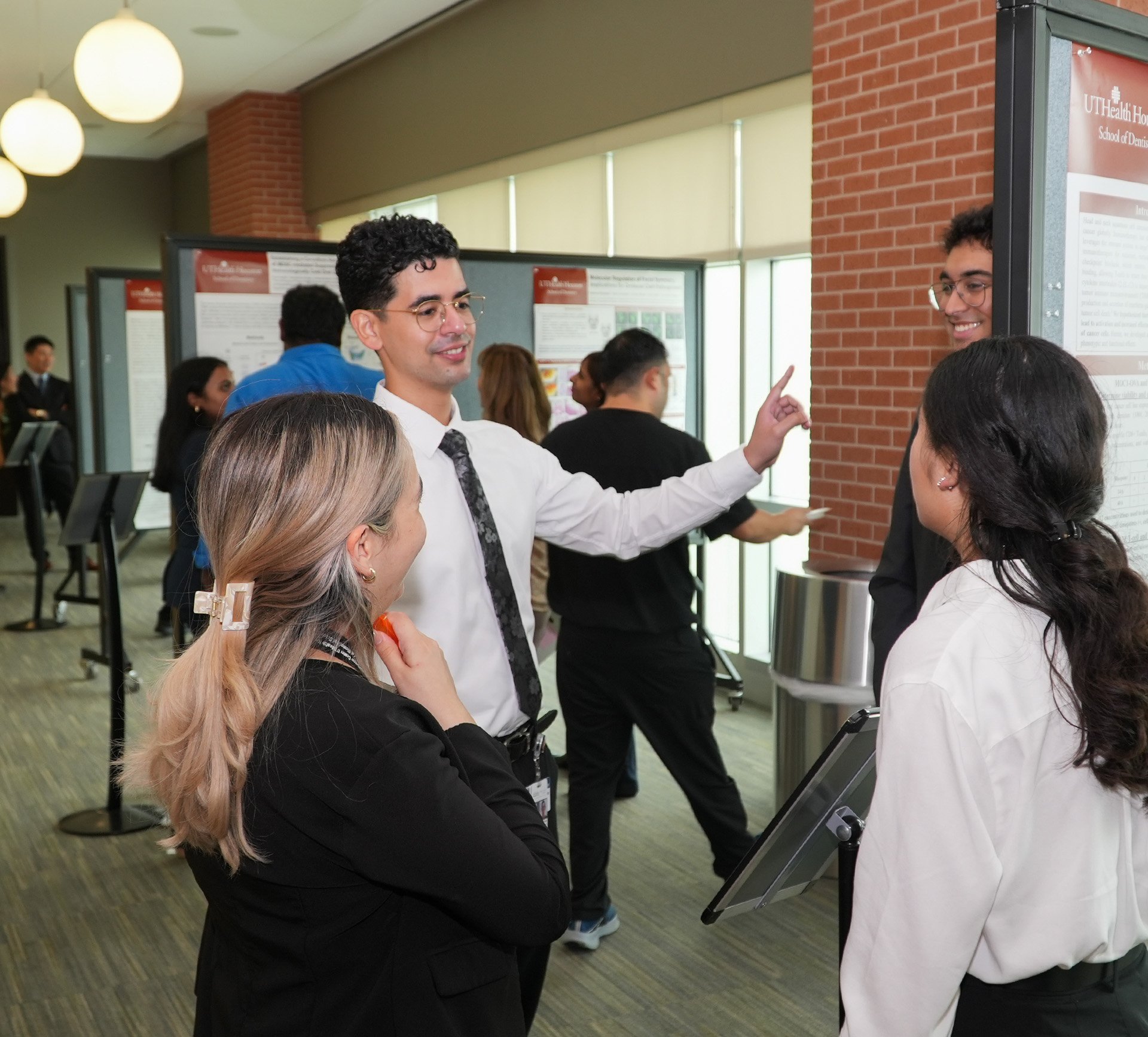 People gathered in a hallway near poster boards, engaged in conversation during an indoor event.