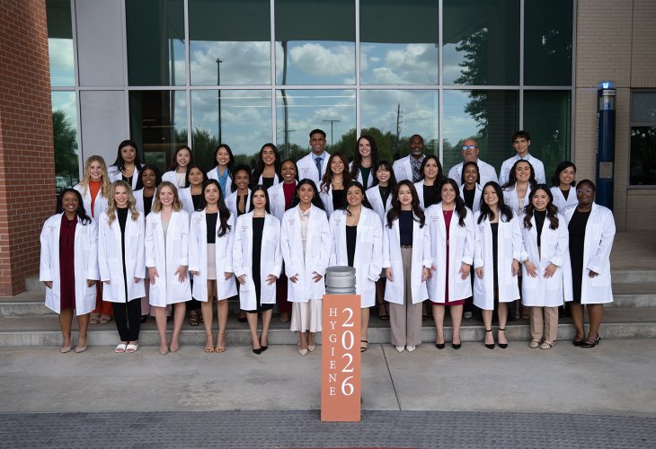Group photo of students wearing white coats on steps.