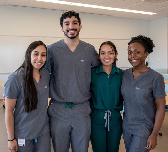 Four people in scrubs interlock arms for a group photo.