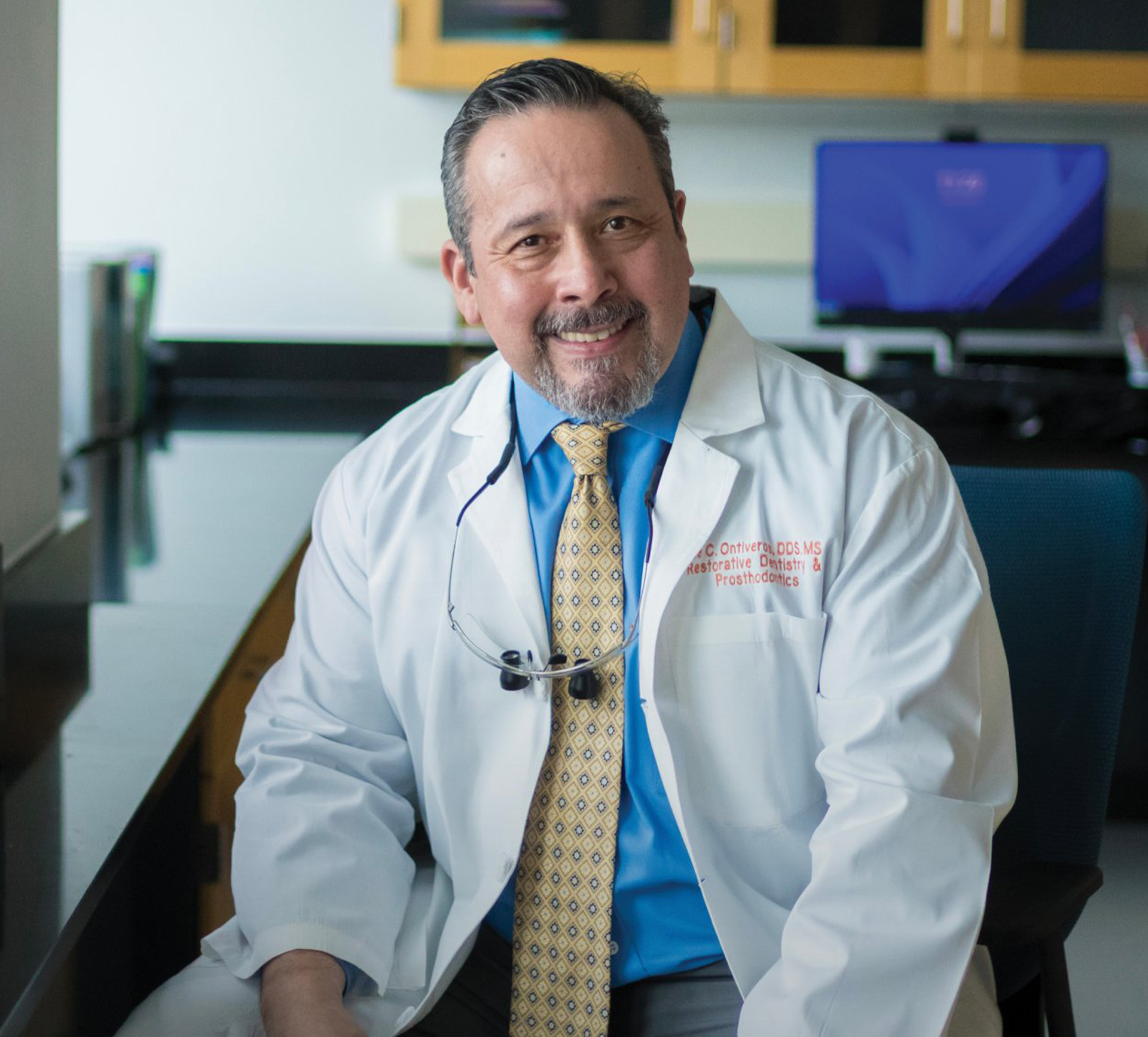 Man in a white coat seated in a laboratory setting.