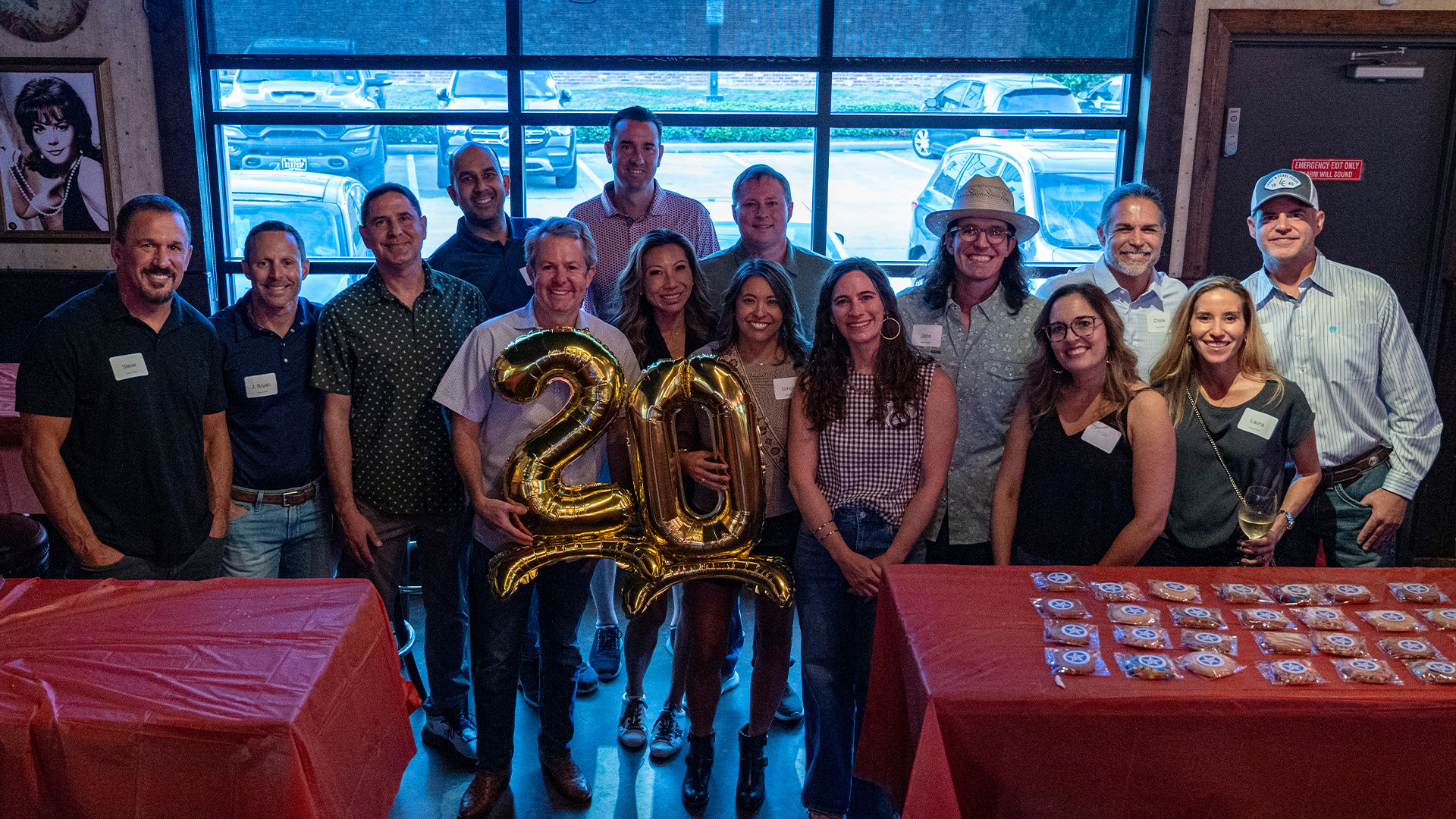 A group of reunion attendees pose indoors behind large gold number balloons during a celebration event.