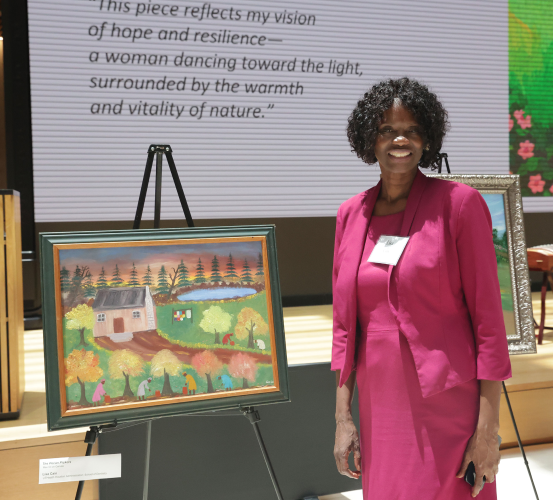 Woman stands next to her painting displayed on an easel at at art exhibition.