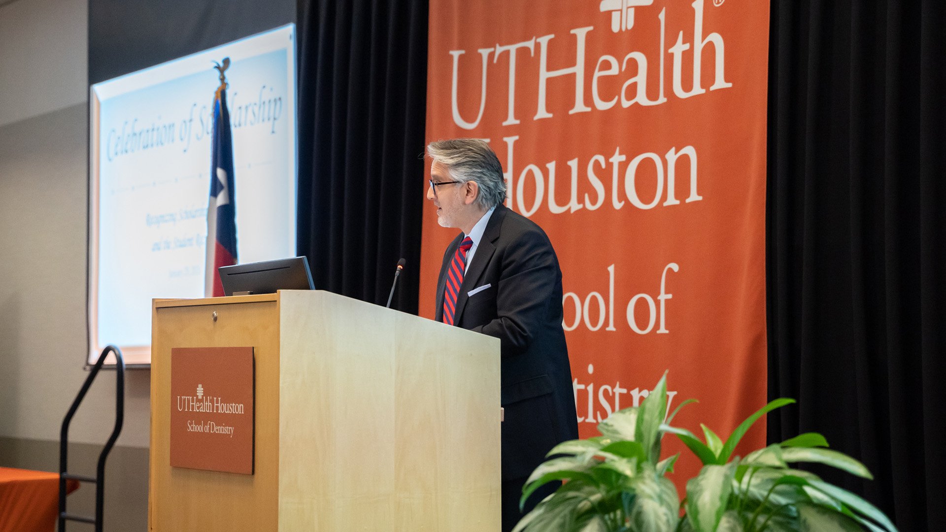 A person stands at a podium giving remarks in front of a UTHealth Houston School of Dentistry backdrop.