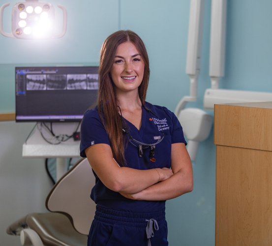 Dental student poses in front of a patient chair.