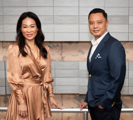 Vinh “Danny” Nguyen DDS, RDH (right), and his wife, Kristy, stand in front of the donor wall at UTHealth Houston School of Dentistry.