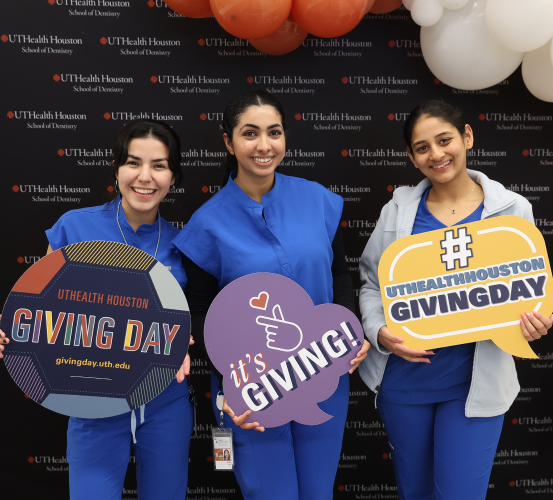 Three dental students hold up event signage for UTHealth Houston Giving Day.