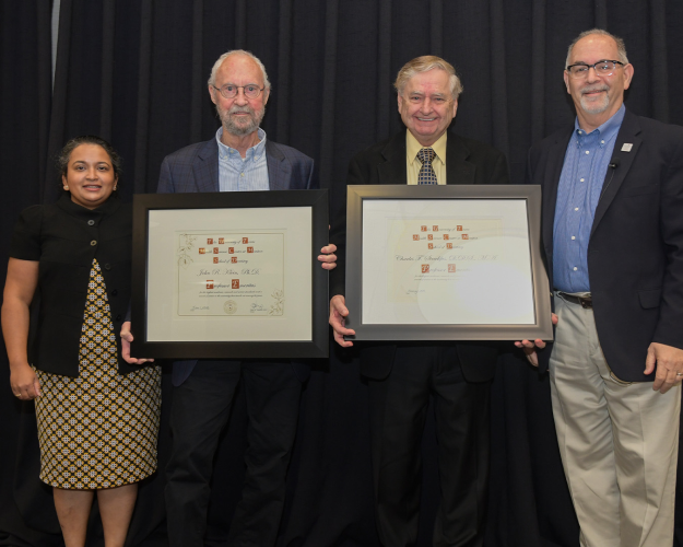 Two men pose with commemorative plaques alongside colleagues.