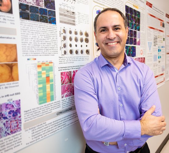 Dr. Walid Fakhouri stands next to his salivary gland poster in the hallway at UTHealth Houston School of Dentistry.