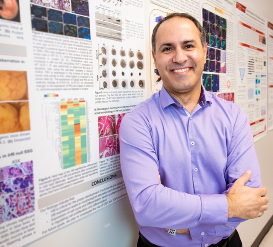 Dr. Walid Fakhouri stands next to his salivary gland poster in the hallway at UTHealth Houston School of Dentistry.