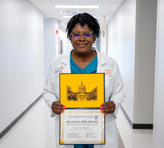 A woman holds a certificate while standing in a hallway.