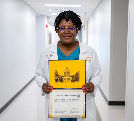 A woman holds a certificate while standing in a hallway.