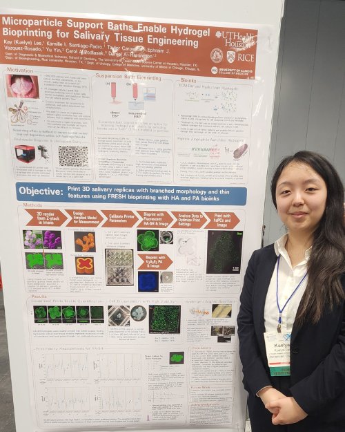 Woman dressed in business casual attire stands next to displayed poster.