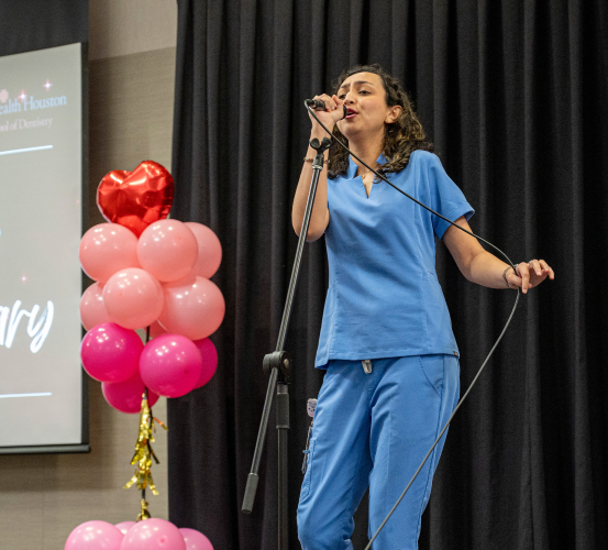 Girl in scrubs sings into a microphone.