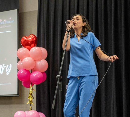 Girl in scrubs sings into a microphone.