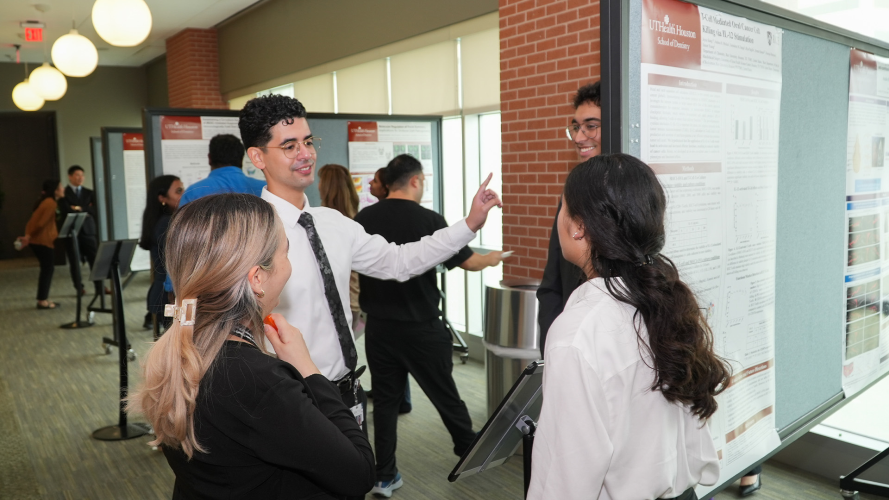 People gathered in a hallway near poster boards, engaged in conversation during an indoor event.