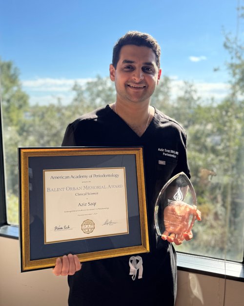Man in scrubs holds an award and certificate.