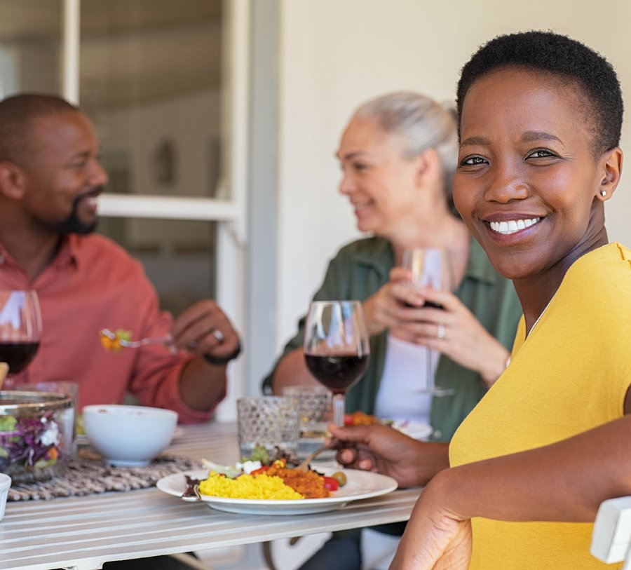 Smiling black woman at dinner with grey-haired white woman and a black man.