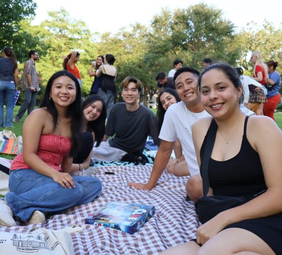 Group of people sit on a picnic blanket in a park.