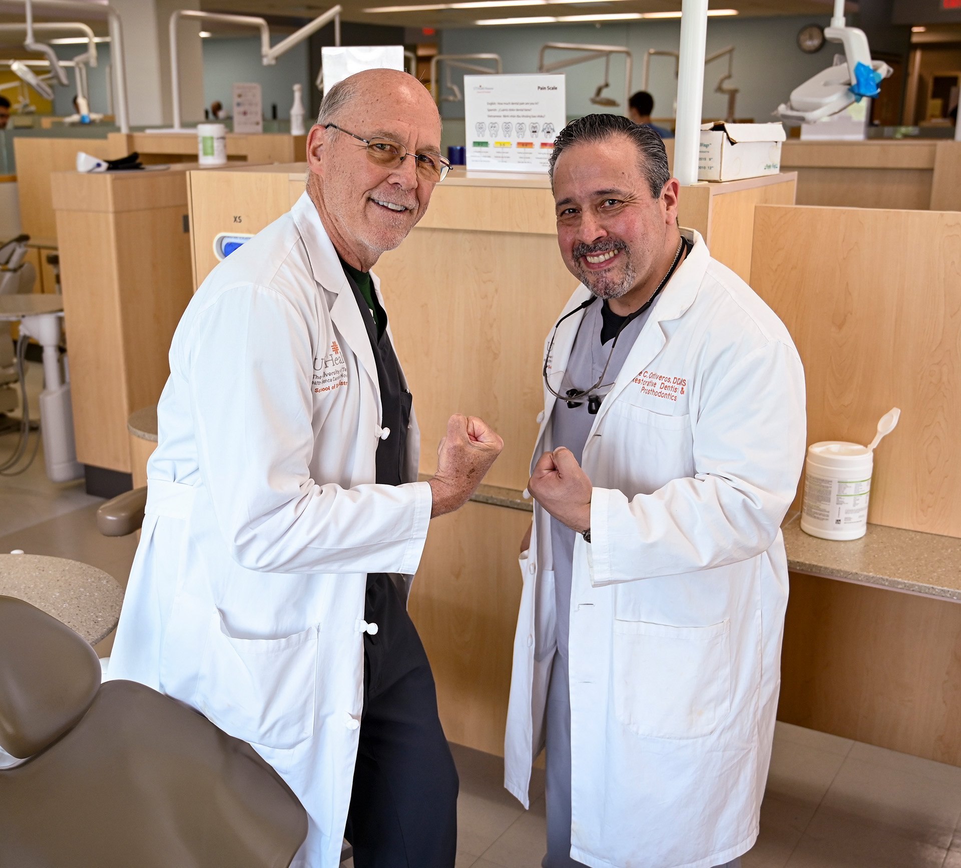 Two dentists in their white coats flexing their biceps.