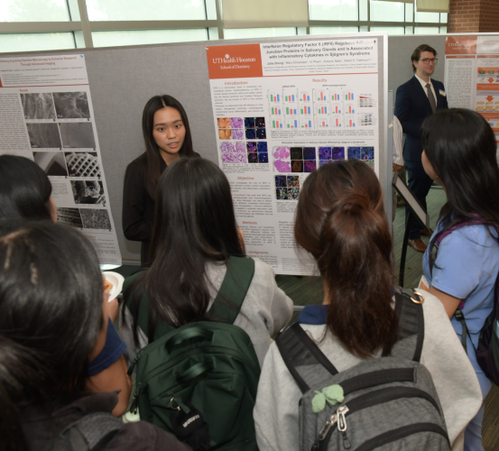 Student presents research findings from a poster to a crowd of five others.