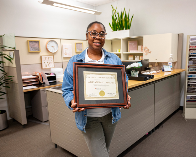 Woman holds an award standing in front of her desk.