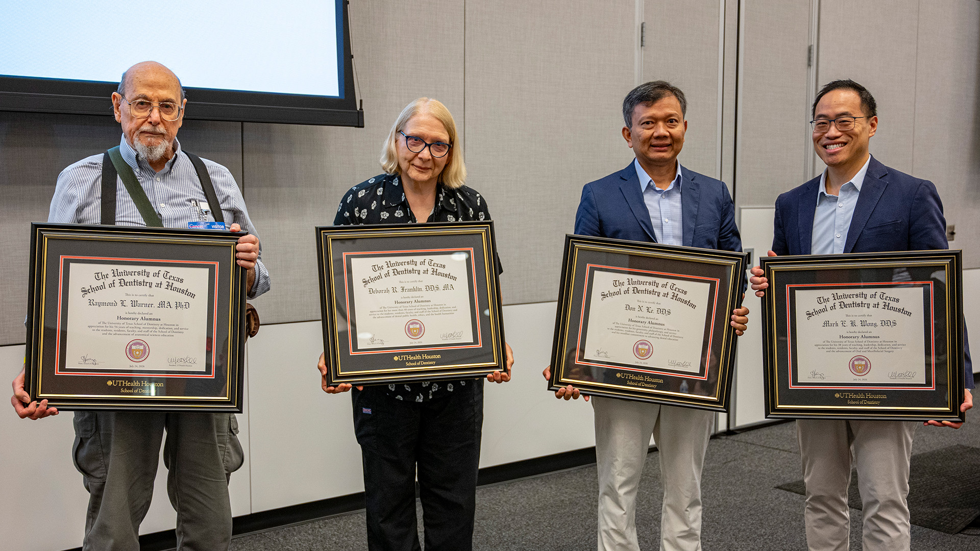 Four individuals stand indoors holding framed Honorary Alumni certificates from UTHealth Houston School of Dentistry .